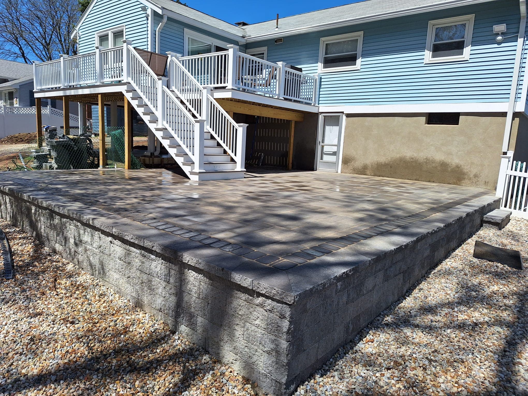Large elevated paver patio behind a blue Cape Cod home