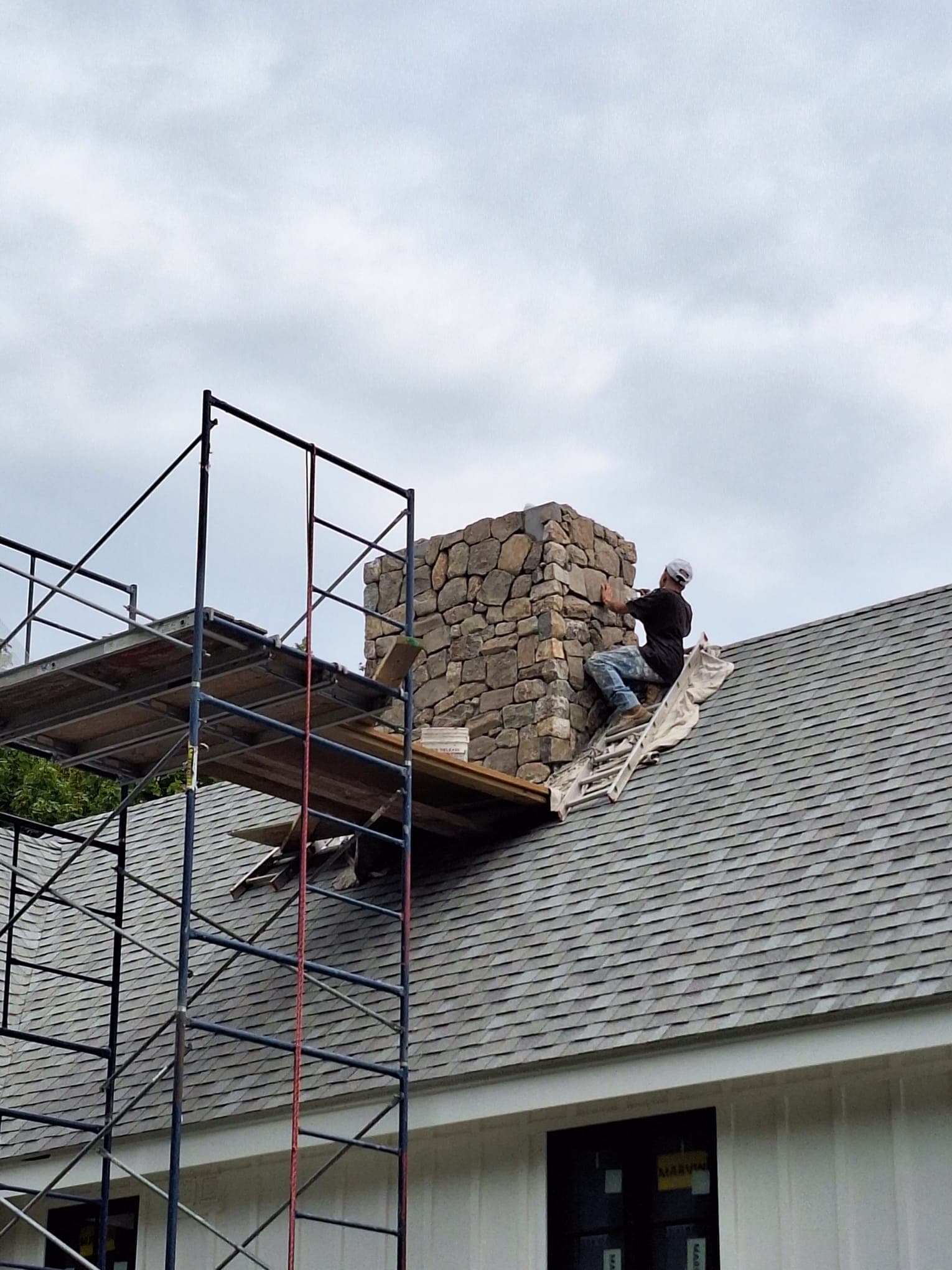 Mason rebuilding a stone chimney from scaffolding on a residential roof